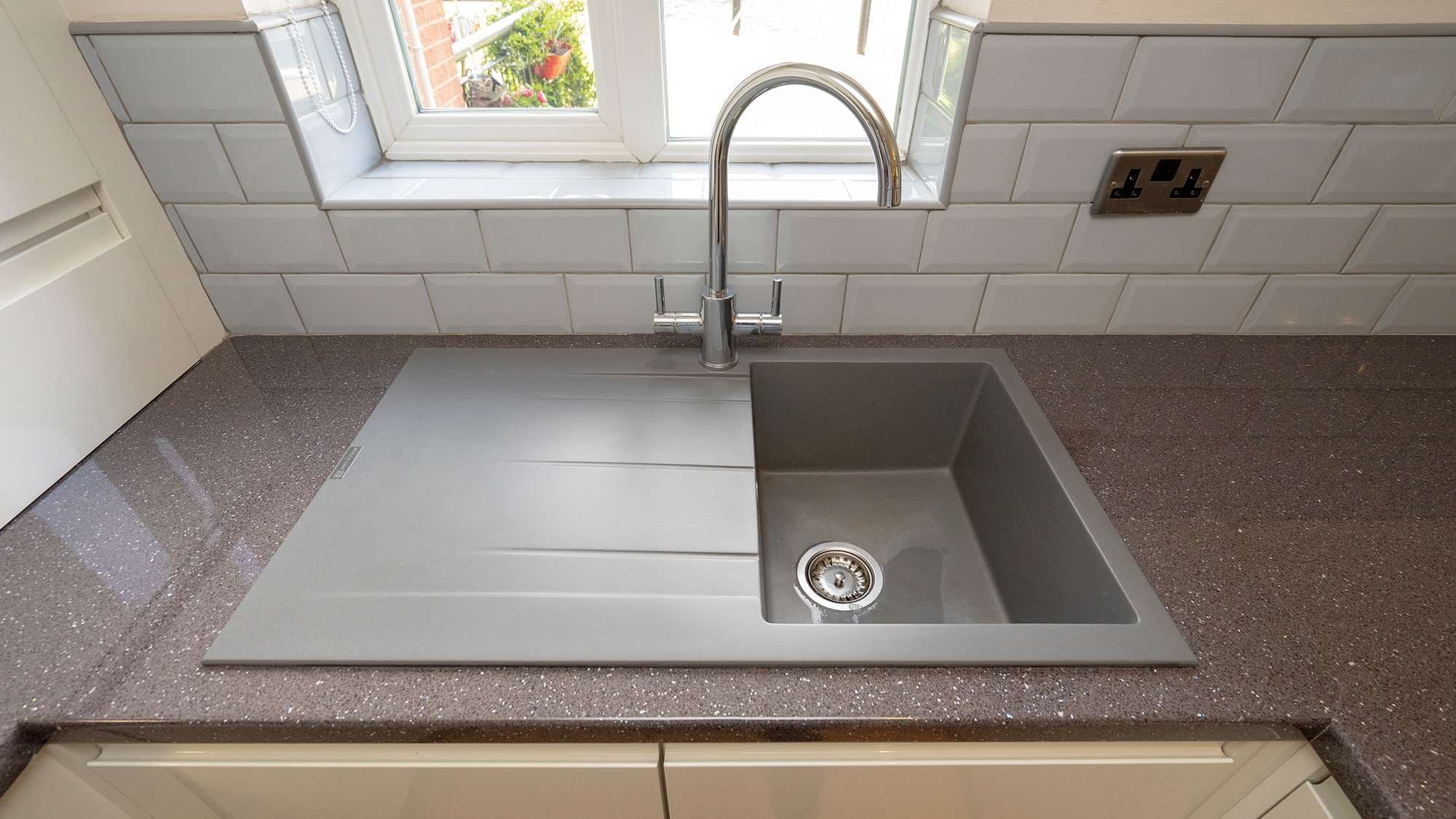 Close up of the sink with a large bowl and draining board, the grey grout used throughout the tiling ties in will with the sink.