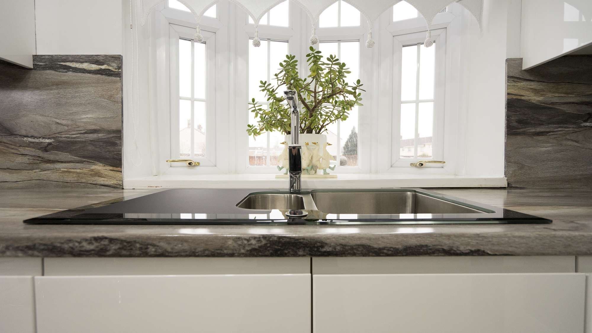 Close up view of a black glass and stainless steel kitchen sink.