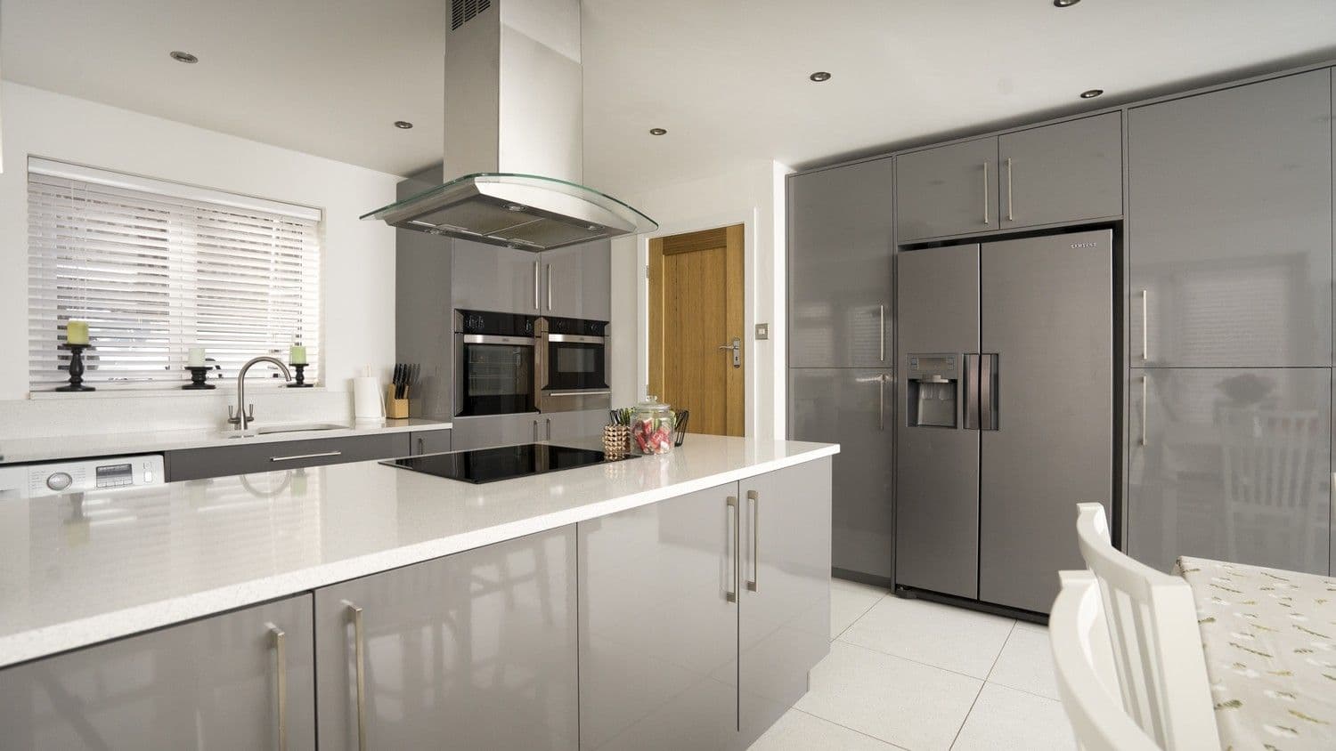 Grey gloss kitchen with overhanging extractor fan and cooking hob and Corian work surfaces.
