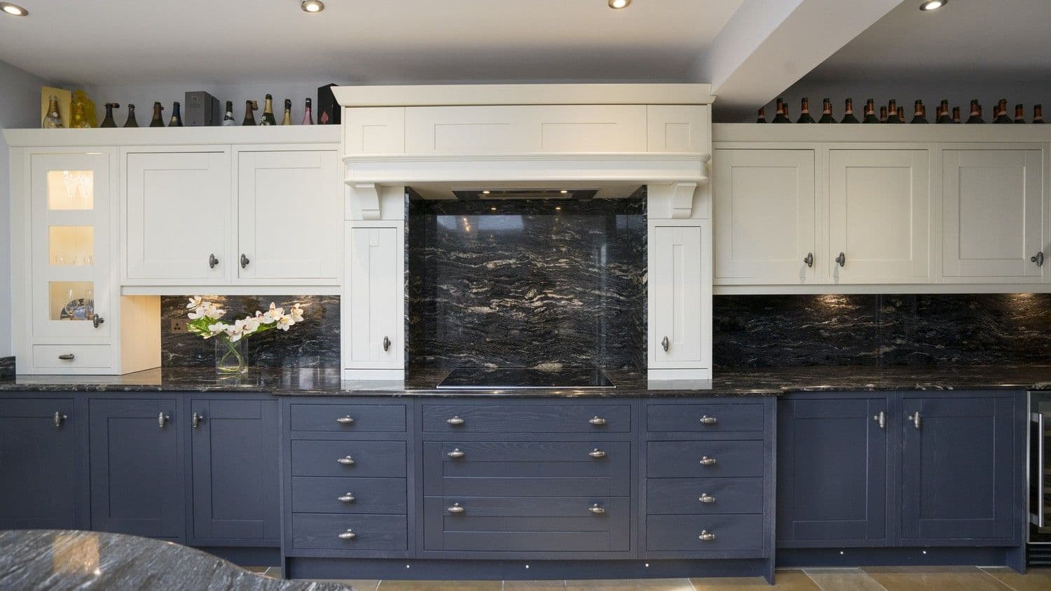 Straight on shot showing the custom mantel details and stunning granite splash backs featuring several Alternative angle showing the feature wall of cupboards housing the multiple Simens oven and a range of different storage solutions. This kitchen features a various built in appliances including extractor fan and large glass hob all from our Liverpool warehouse.