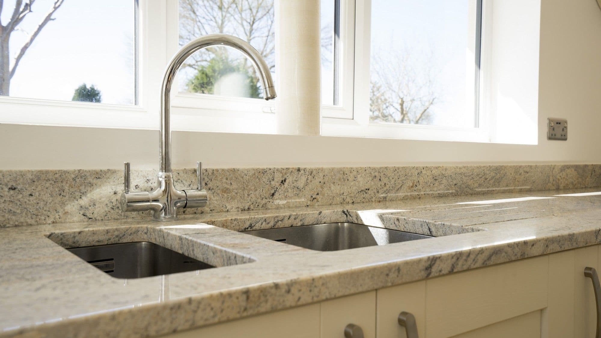 Close up of the stainless steel sink and tap, under-mounted to the granite worktops.