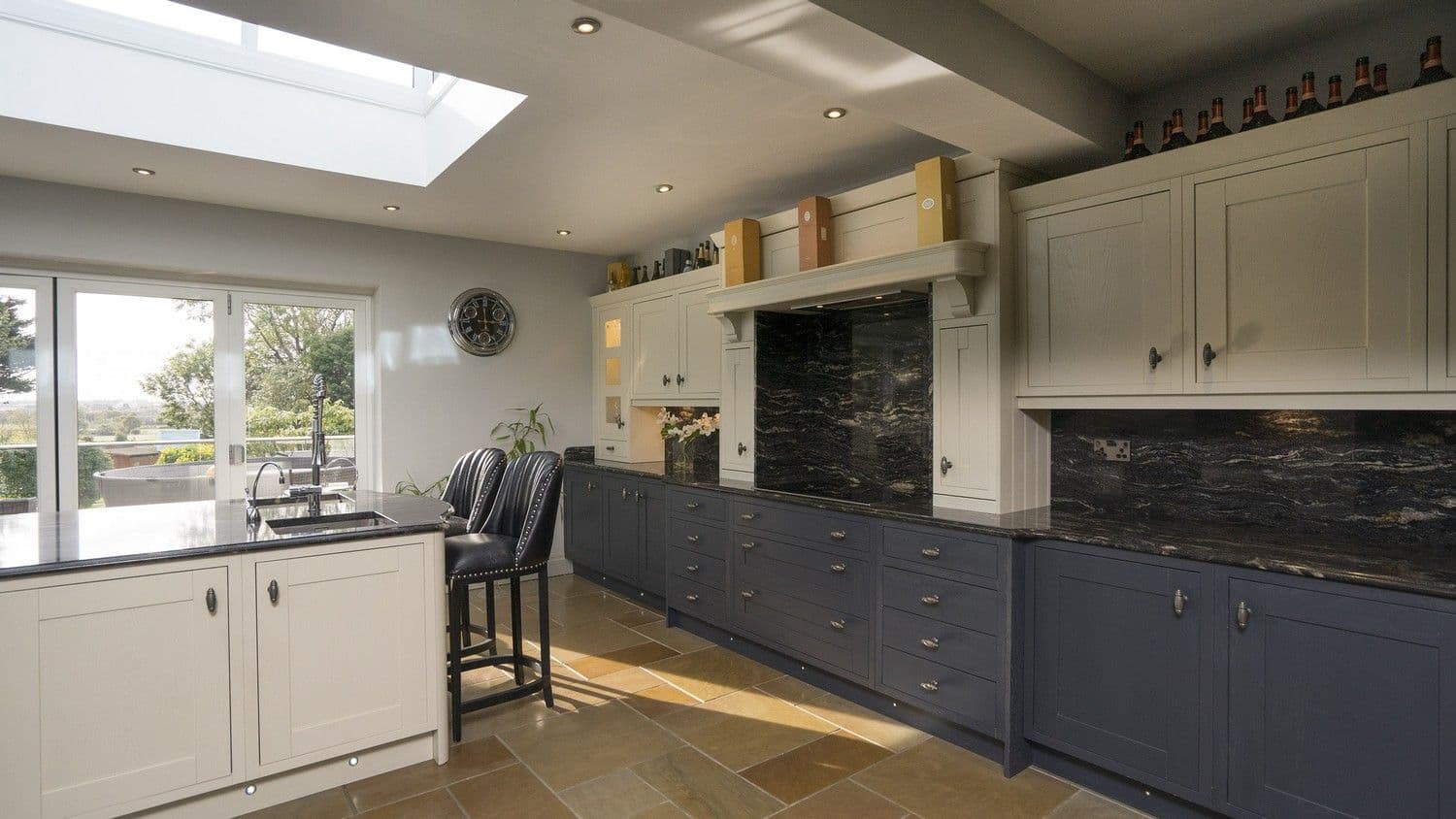 Two tone expertly designed timber In-frame kitchen installed for our clients in Ormskirk featuring a variety of cupboards and draws with aged metal handles and granite worktops. Images shows stunning views from the kitchen through the bifold doors, the bifold doors and roof lantern flood this kitchen with lots of natural light making it a real feature of this home.