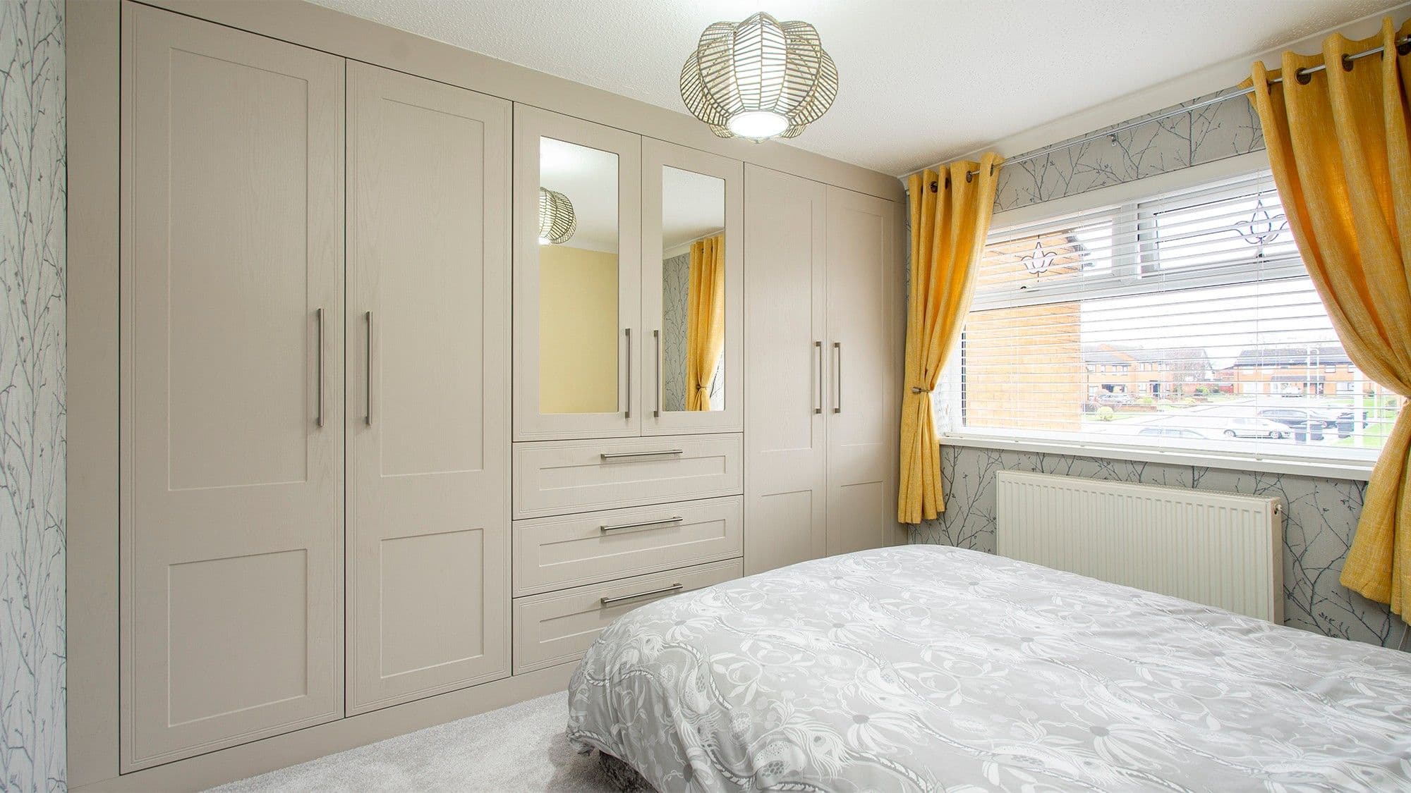 Shaker style fitted wardrobes with centre drawers and mirrored doors. Matching top, bottom and side panelling gives the wardrobe a fully fitted finish.