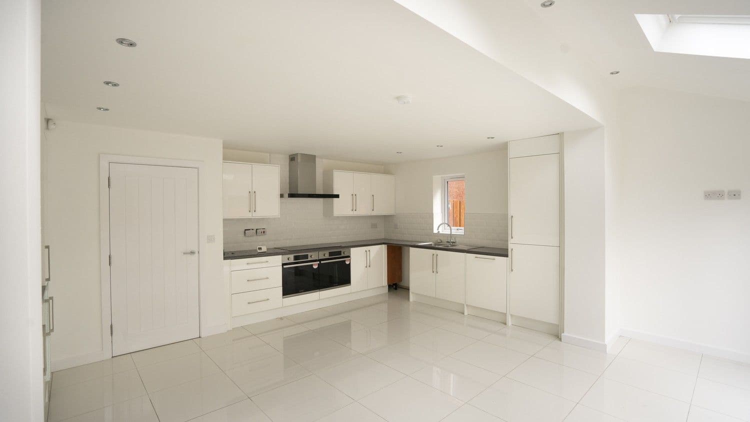 Gloss white kitchen installed featuring dual ovens, integrated appliances, lots of storage space and a large extractor fan.