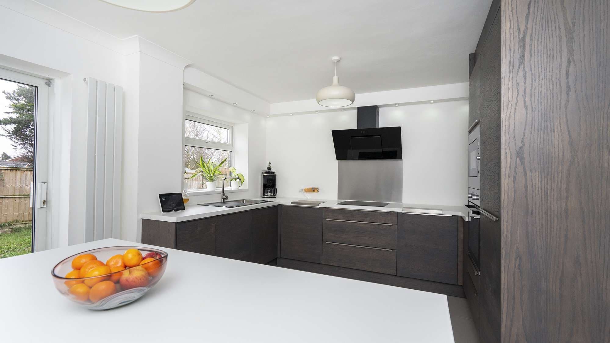 Alternative view of this modern walnut slab kitchen with white worktops and stainless steel accents.