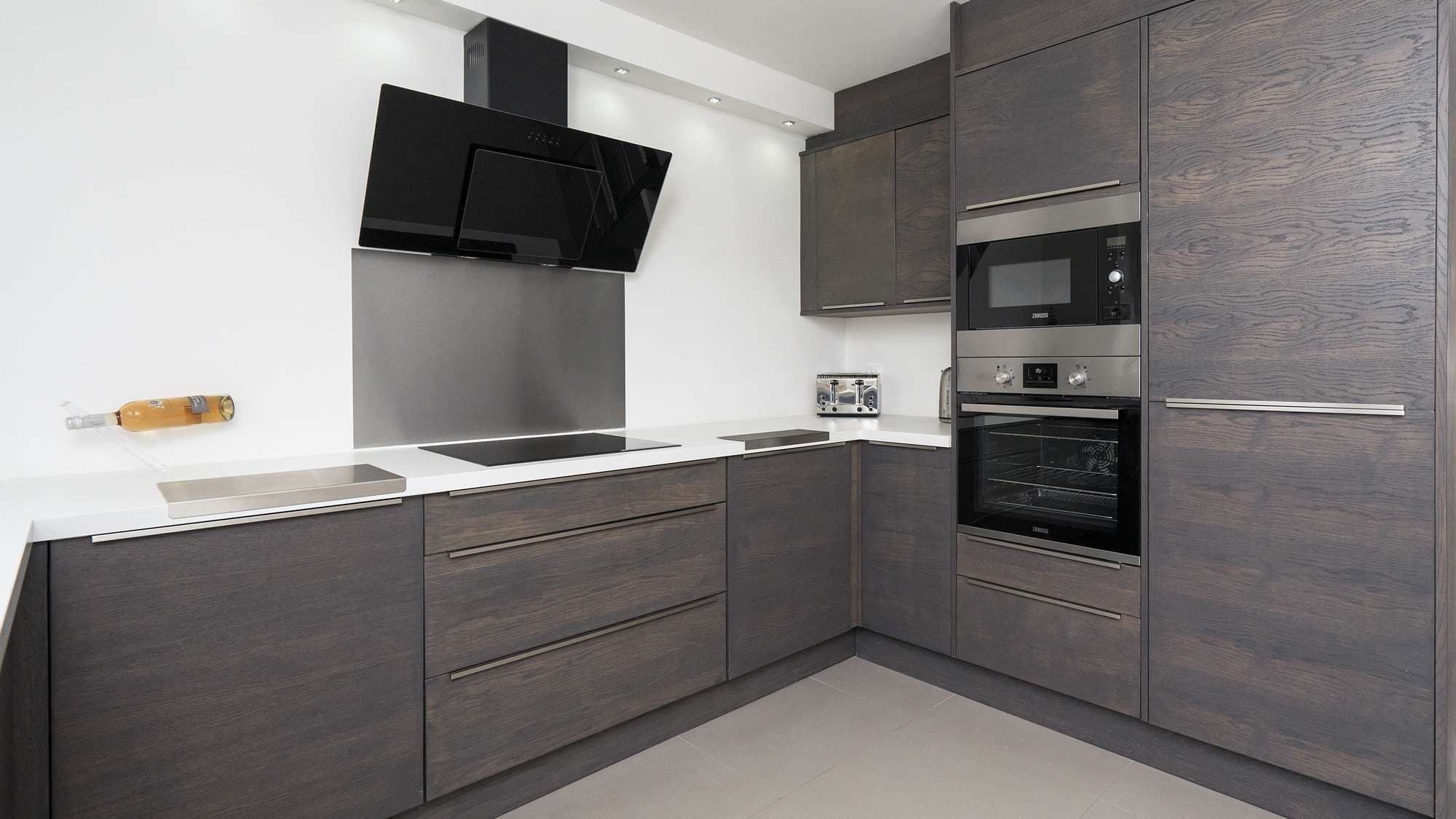 Close up of the cooking area with built in oven, microwave and ceramic hob. Large black extractor above the hob.
