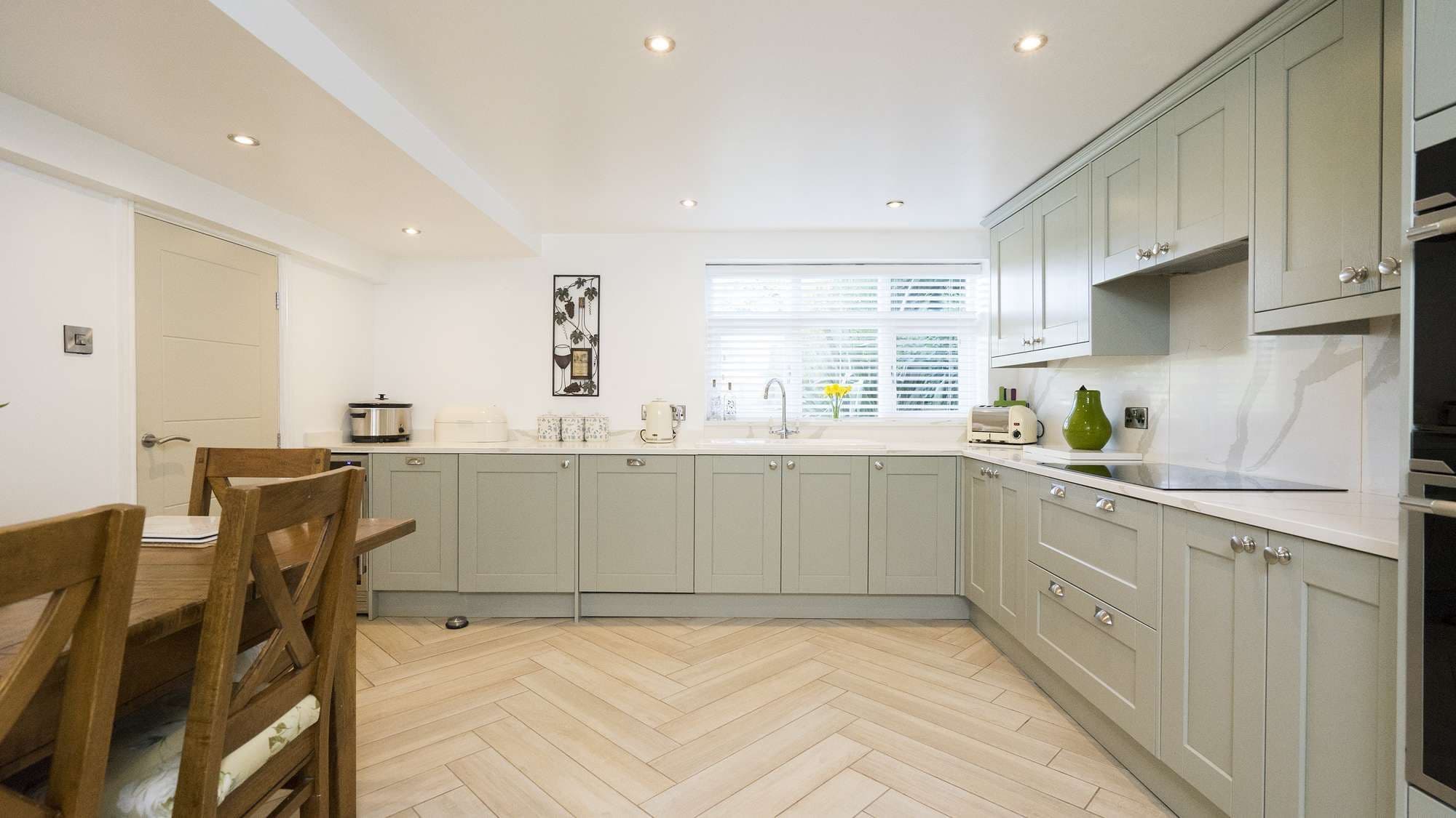 Straight on view of this large shaker kitchen in olive green with white marble style worktops and matching backsplashes.